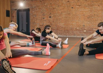 A group of diverse adults stretching on mats in a brick-walled fitness studio.