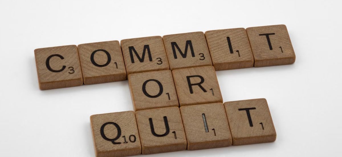 Wooden Scrabble tiles arranged to form the words 'Commit or Quit' on a white background.