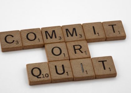 Wooden Scrabble tiles arranged to form the words 'Commit or Quit' on a white background.